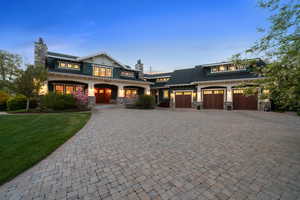 View of front of home with a chimney, stone siding, a yard, and decorative driveway