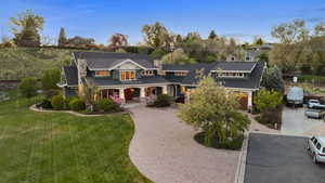 Shingle-style home with a chimney, decorative driveway, a shingled roof, a porch, and a front lawn