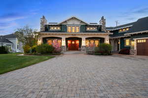 View of front of home featuring stone siding, decorative driveway, a chimney, and a porch