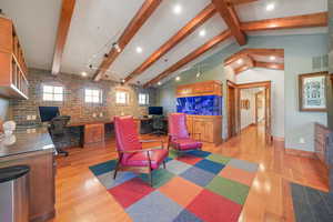 Living area with visible vents, light wood-style flooring, lofted ceiling with beams, and brick wall