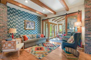 Living room featuring wood finished floors, a barn door, recessed lighting, brick wall, and vaulted ceiling with beams