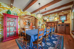 Dining space featuring a notable chandelier, wallpapered walls, wood finished floors, arched walkways, and beam ceiling