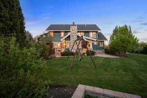 Back of house at dusk featuring a chimney and a lawn