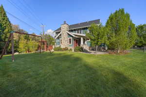 Back of property featuring a chimney, a yard, stone siding, and fence