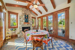 Dining space with brick floor, lofted ceiling with beams, french doors, a fireplace, and ceiling fan