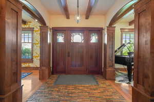 Entrance foyer featuring beam ceiling, brick floor, and decorative columns