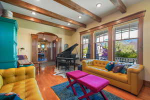 Living room with beam ceiling, wood finished floors, decorative columns, recessed lighting, and arched walkways