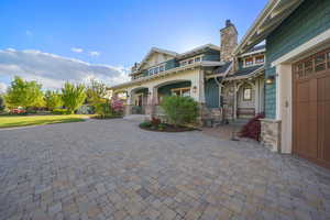 Craftsman-style home with a porch, curved driveway, a chimney, and stone siding