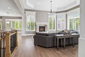Living area with a tray ceiling, a fireplace, hardwood / wood-style floors, a notable chandelier, and baseboards