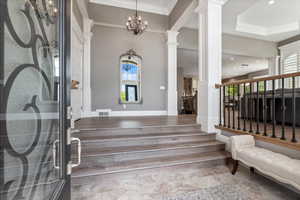 Entrance foyer featuring visible vents, decorative columns, a chandelier, crown molding, and stairway