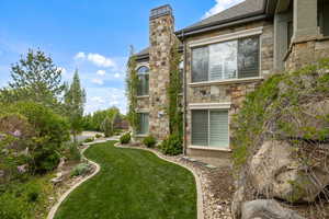 View of home's exterior featuring a lawn, stone siding, roof with shingles, and a chimney