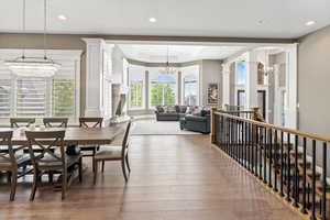 Dining space with an inviting chandelier, ornate columns, a tray ceiling, hardwood / wood-style flooring, and recessed lighting