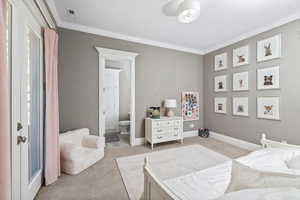 Bedroom with crown molding, ensuite bathroom, light carpet, and visible vents