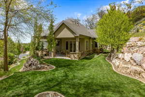 Back of house with stone siding, a patio, stucco siding, a yard, and roof with shingles