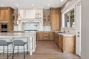 Kitchen featuring glass insert cabinets, light wood finished floors, a sink, stainless steel appliances, and tasteful backsplash