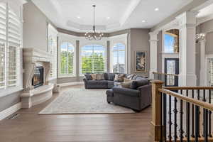 Living room featuring a raised ceiling, a notable chandelier, a fireplace, and wood finished floors