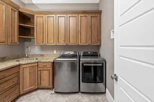 Clothes washing area featuring a sink, cabinet space, light tile patterned flooring, and washing machine and clothes dryer