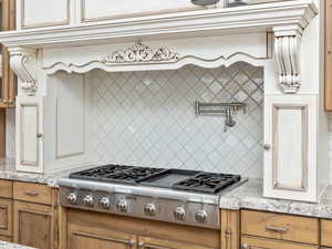 Kitchen with brown cabinets, stainless steel gas stovetop, light wood-type flooring, backsplash, and light stone countertops