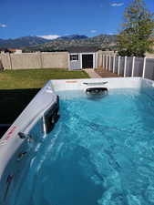 View of swimming pool with a fenced backyard, an outdoor structure, a mountain view, and a lawn