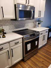 Kitchen featuring white cabinets, backsplash, dark wood-style floors, and appliances with stainless steel finishes
