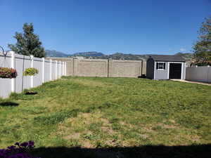 View of yard featuring a fenced backyard, an outbuilding, a mountain view, and a storage shed