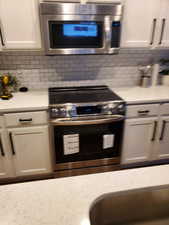 Kitchen with light countertops, appliances with stainless steel finishes, decorative backsplash, and white cabinetry