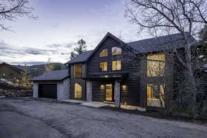 View of front of house featuring driveway, a standing seam roof, faux log siding, an attached garage, and stone siding