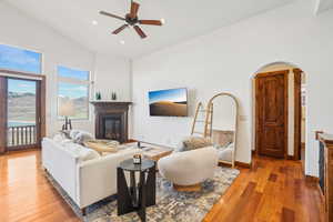 Living area with light wood-type flooring, high vaulted ceiling, ceiling fan, arched walkways, and a glass covered fireplace