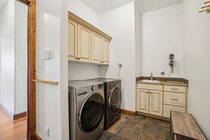 Washroom with cabinet space, washer and clothes dryer, baseboards, and a sink