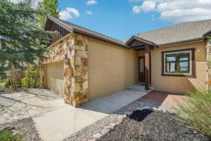 Property entrance with roof with shingles, an attached garage, stone siding, stucco siding, and board and batten siding