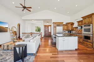Kitchen with a breakfast bar area, brown cabinetry, open floor plan, light wood-style floors, and appliances with stainless steel finishes
