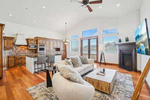 Living area with recessed lighting, ceiling fan with notable chandelier, high vaulted ceiling, a fireplace, and light wood-type flooring