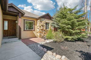 View of exterior entry with stone siding, board and batten siding, stucco siding, and roof with shingles