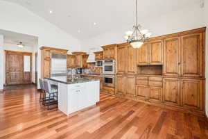 Kitchen with light wood-style flooring, a breakfast bar, high vaulted ceiling, a notable chandelier, and built in appliances