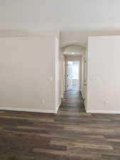 Hall with a textured ceiling, arched walkways, dark wood-type flooring, and baseboards