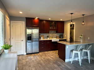 Kitchen featuring glass insert cabinets, a kitchen bar, stainless steel refrigerator with ice dispenser, light wood-style floors, and tasteful backsplash