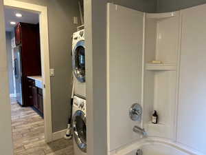 Laundry area featuring laundry area, stacked washer and dryer, baseboards, and light wood finished floors
