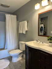 Full bath with washer / clothes dryer, toilet, shower / tub combo with curtain, visible vents, and vanity