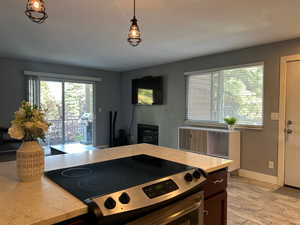 Kitchen with light stone countertops, light wood-style flooring, baseboards, hanging light fixtures, and electric range