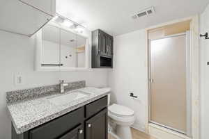 Bathroom with a stall shower, toilet, visible vents, vanity, and wood finished floors