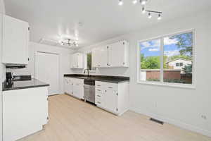 Kitchen featuring range, dishwasher, visible vents, a sink, and white cabinetry