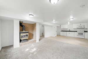 Unfurnished living room featuring a wood stove, a textured ceiling, light carpet, and baseboards