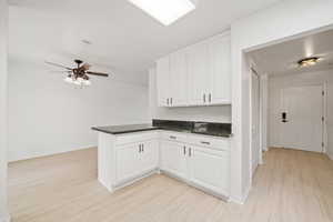 Kitchen featuring a ceiling fan, baseboards, white cabinetry, a peninsula, and light wood-style floors