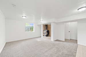 Unfurnished living room featuring crown molding, a wood stove, a textured ceiling, and carpet