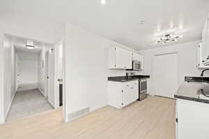Kitchen featuring appliances with stainless steel finishes, visible vents, a sink, white cabinetry, and light wood-type flooring