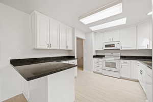 Kitchen with baseboards, white appliances, light wood finished floors, white cabinetry, and a peninsula