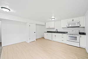 Kitchen featuring baseboards, white appliances, dark countertops, white cabinets, and light wood-type flooring