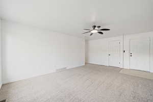 Empty room featuring light colored carpet, visible vents, baseboards, and a ceiling fan