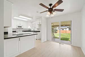 Kitchen featuring white cabinetry, a peninsula, white appliances, and dark countertops