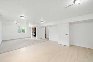 Below grade area featuring a textured ceiling, baseboards, visible vents, and light wood-style floors
